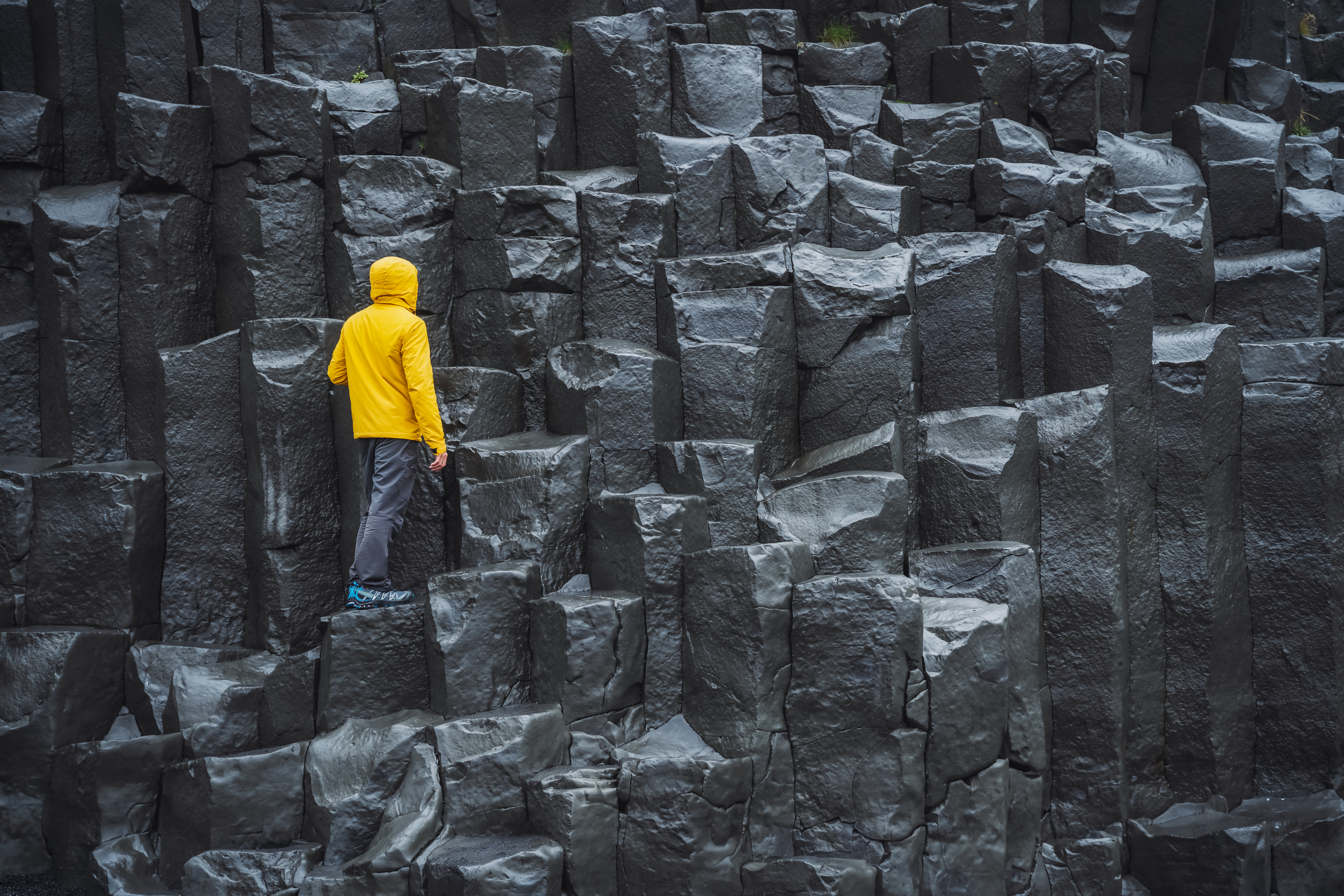 Man wearing yellow coat looking up at Reynisdrangar basalt columns at Reynisfjara Beach, Iceland